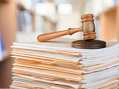 A wooden gavel resting on top of neatly arranged manila folders. The gavel's handle is made of polished wood, and the folders are placed in a stack, ready for use in a professional or legal setting.